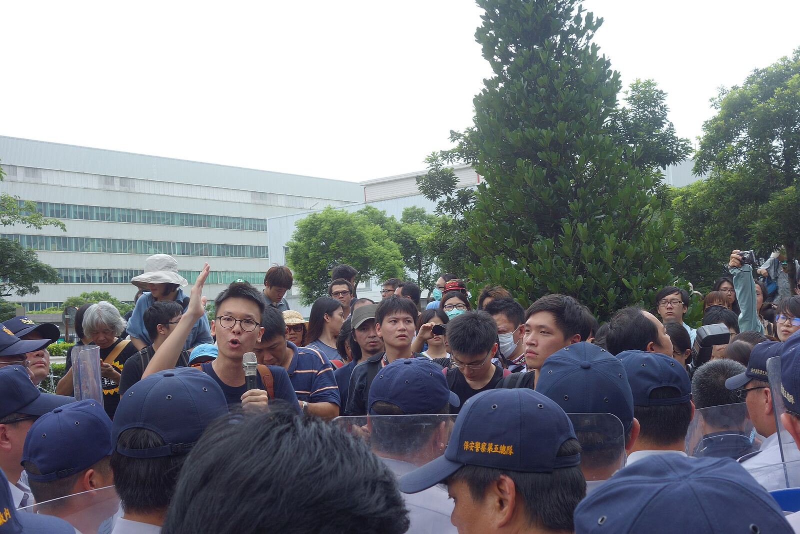 A large group of people gather outdoors wearing blue caps during a protest.