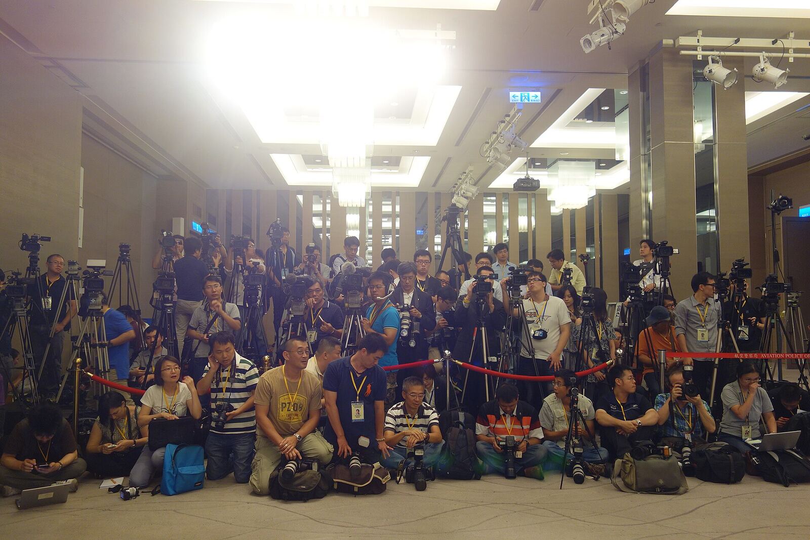 A large group of photographers and journalists gather with cameras at an indoor press conference.