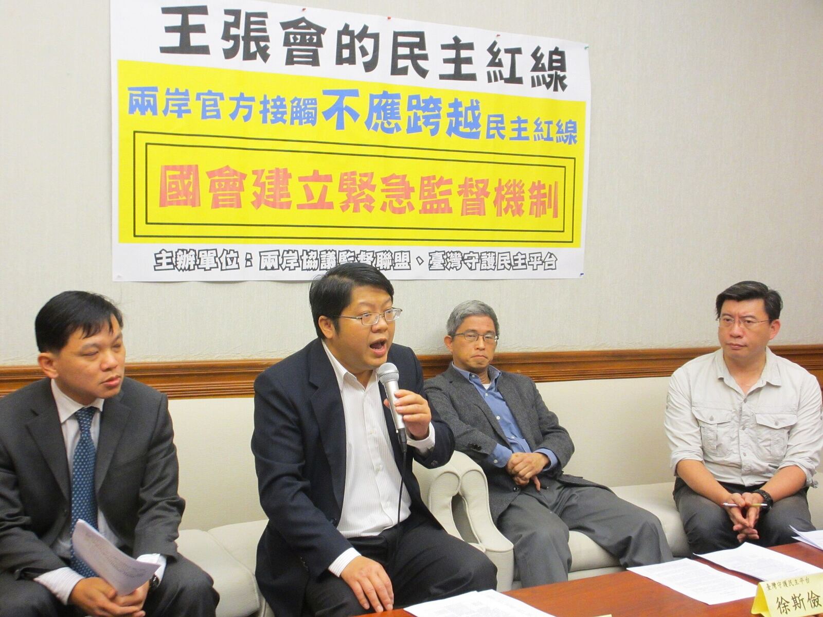 A group of men are seated at a table during a press conference discussing democratic boundaries for cross-strait.